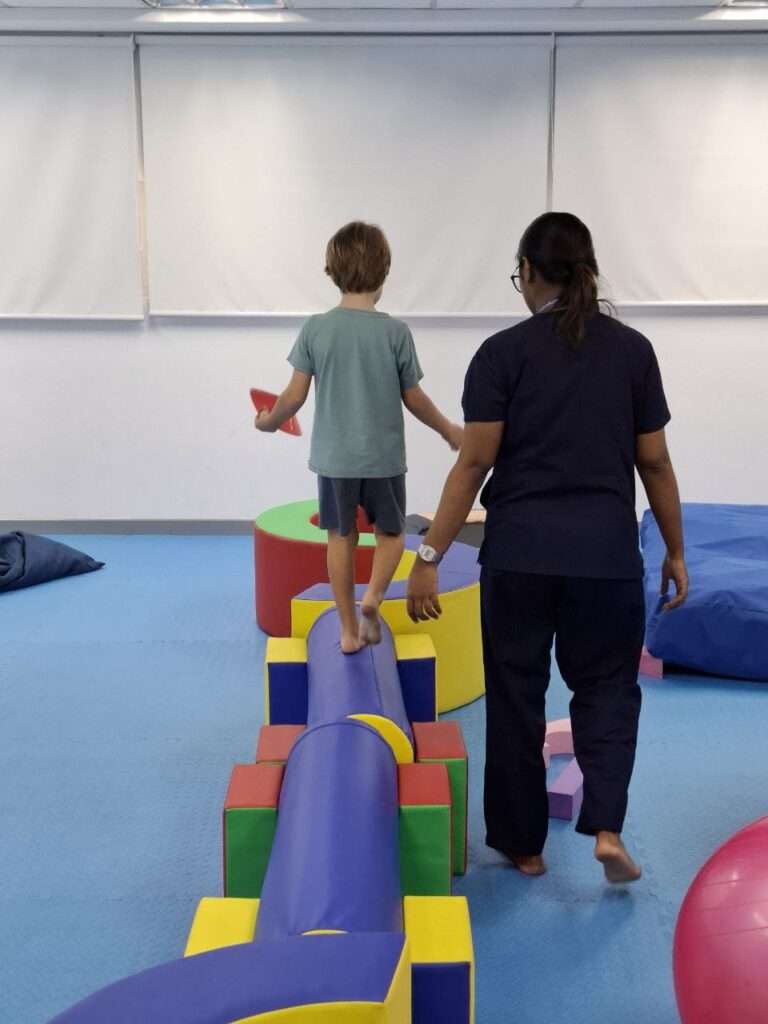 Child practicing balance on a sensory obstacle course with therapist support during an occupational therapy session at OrbRom Center in Phnom Penh.