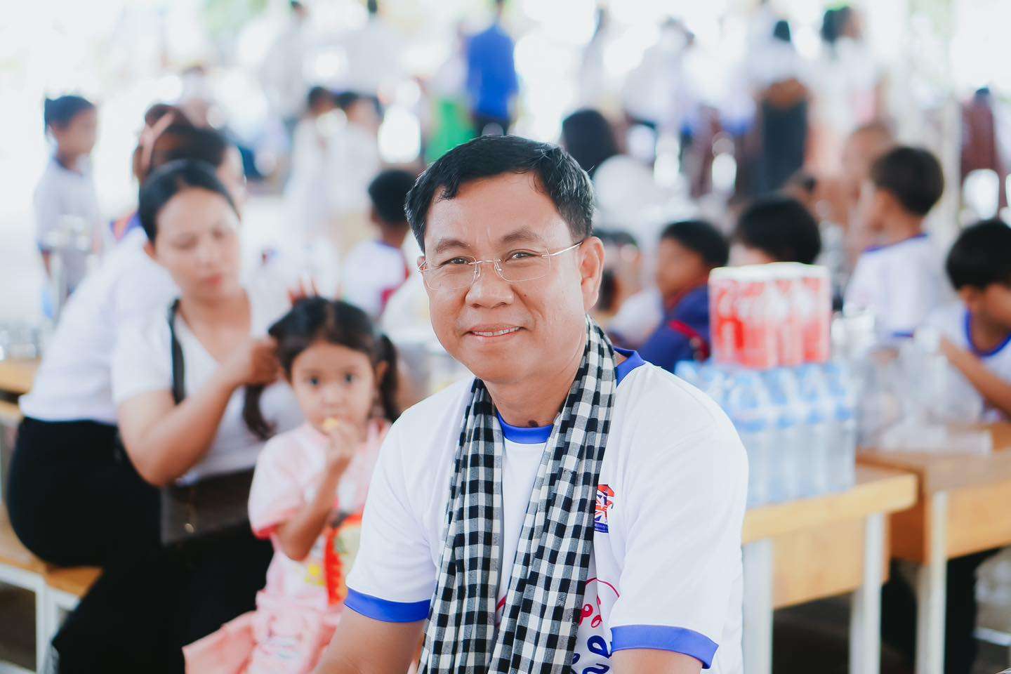 School leader at Western Bridge School Kampong Chhnang smiling during a community event with parents and children in the background.