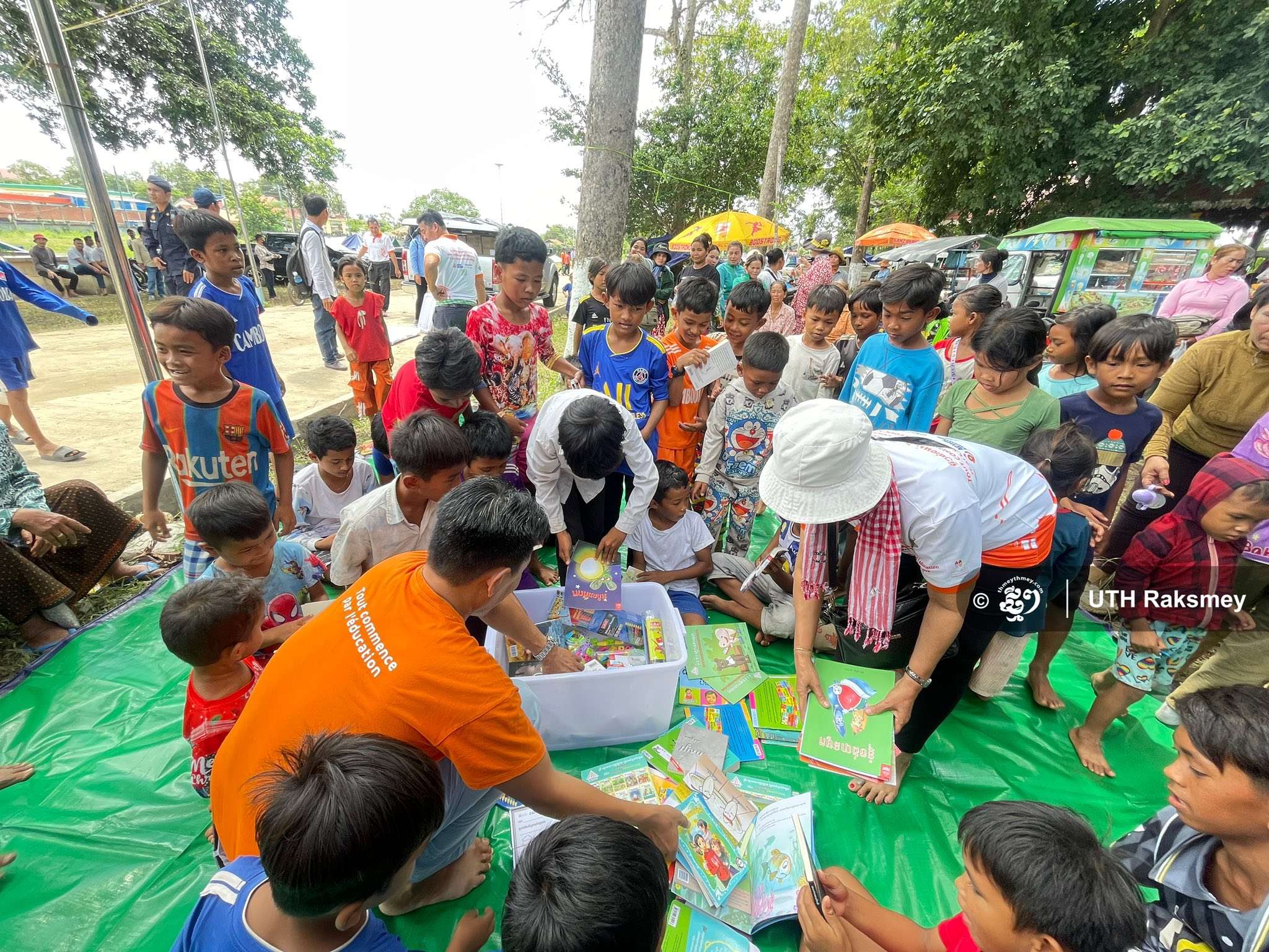 Children reading books together on mats during a literacy outreach event by Aide et Action Cambodia, showcasing joyful learning in a community setting.