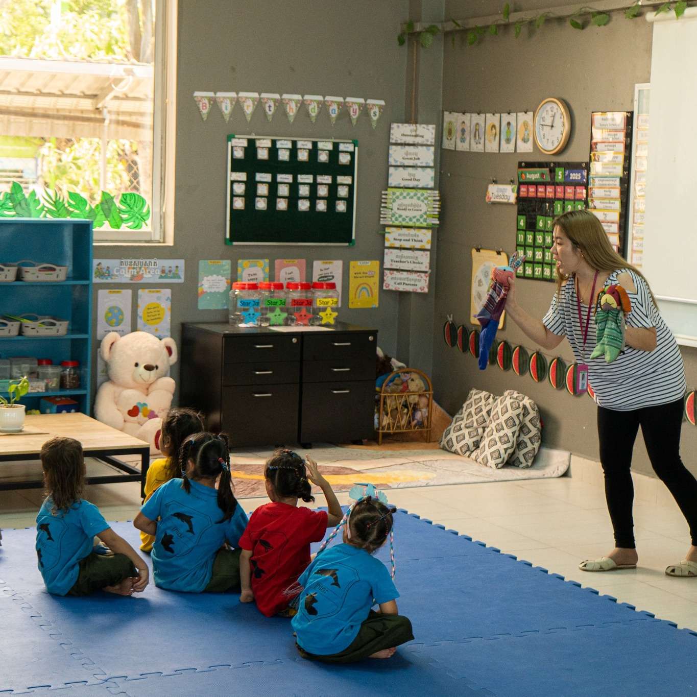 A teacher at Asian Hope International School engaging young children with colorful learning props in a bright, play-based classroom setting.