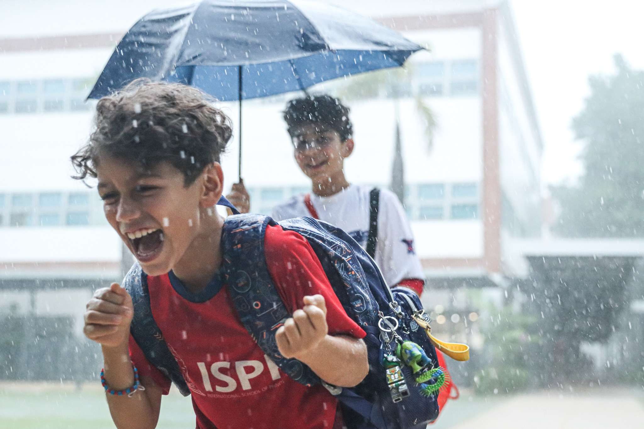 ISPP students running and laughing in the rain on campus, sharing umbrellas and enjoying a spontaneous rainy afternoon together