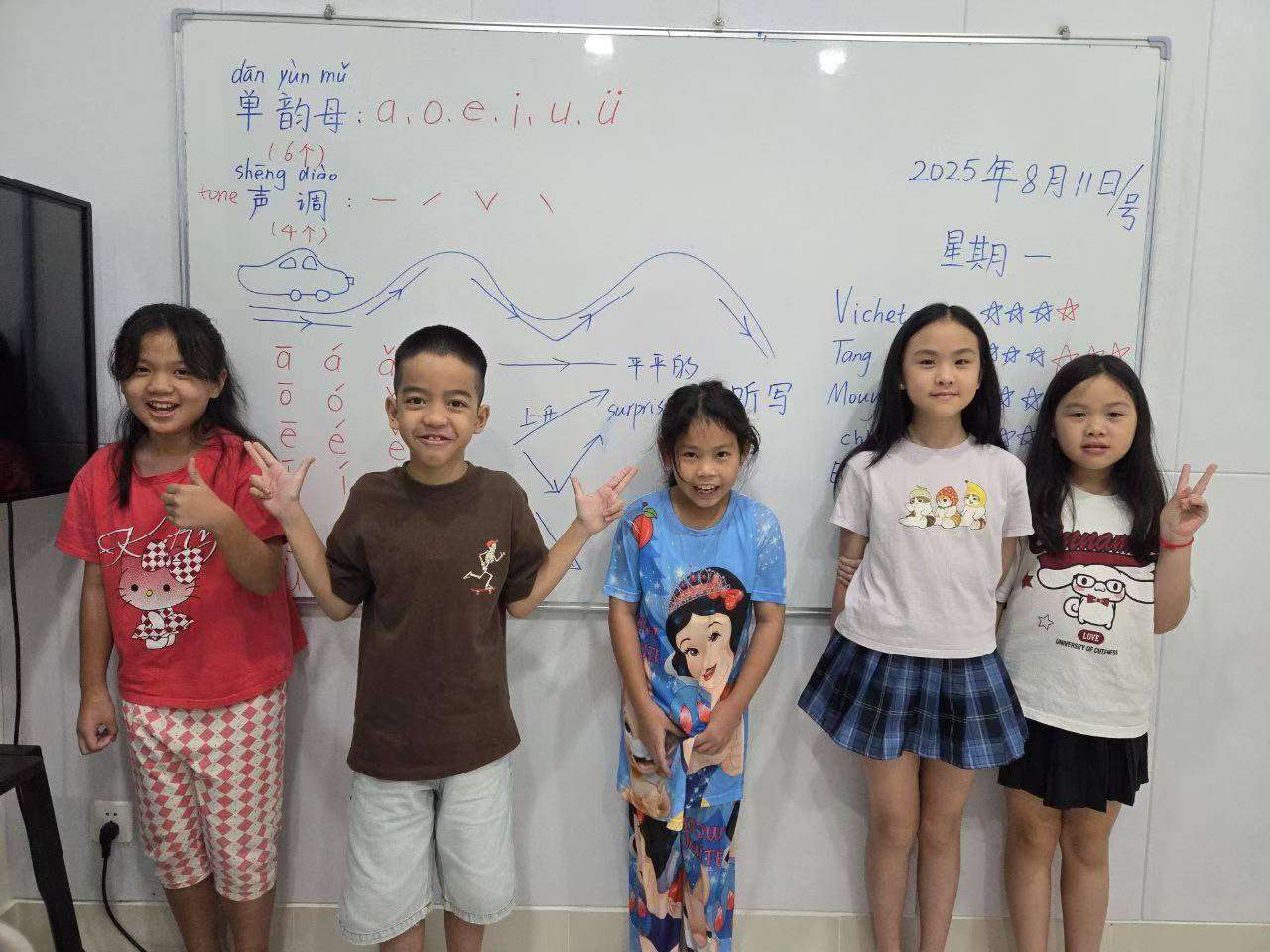 Students at OAK Chinese Education Phnom Penh smiling in class, standing in front of a whiteboard with Chinese writing, showing enthusiasm for learning Mandarin.