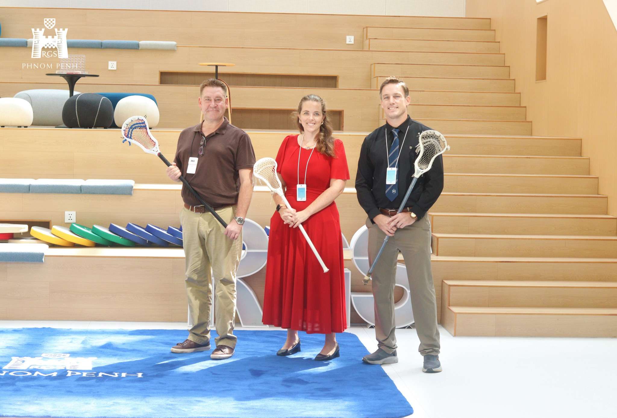 Rob McKee, Joseph Costello, and Caroline Hosegood holding lacrosse sticks during the visit.