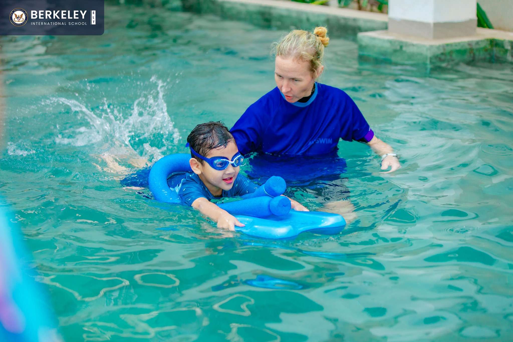 Children at Berkeley International School swimming class with their teacher, enjoying water activities and smiling together.