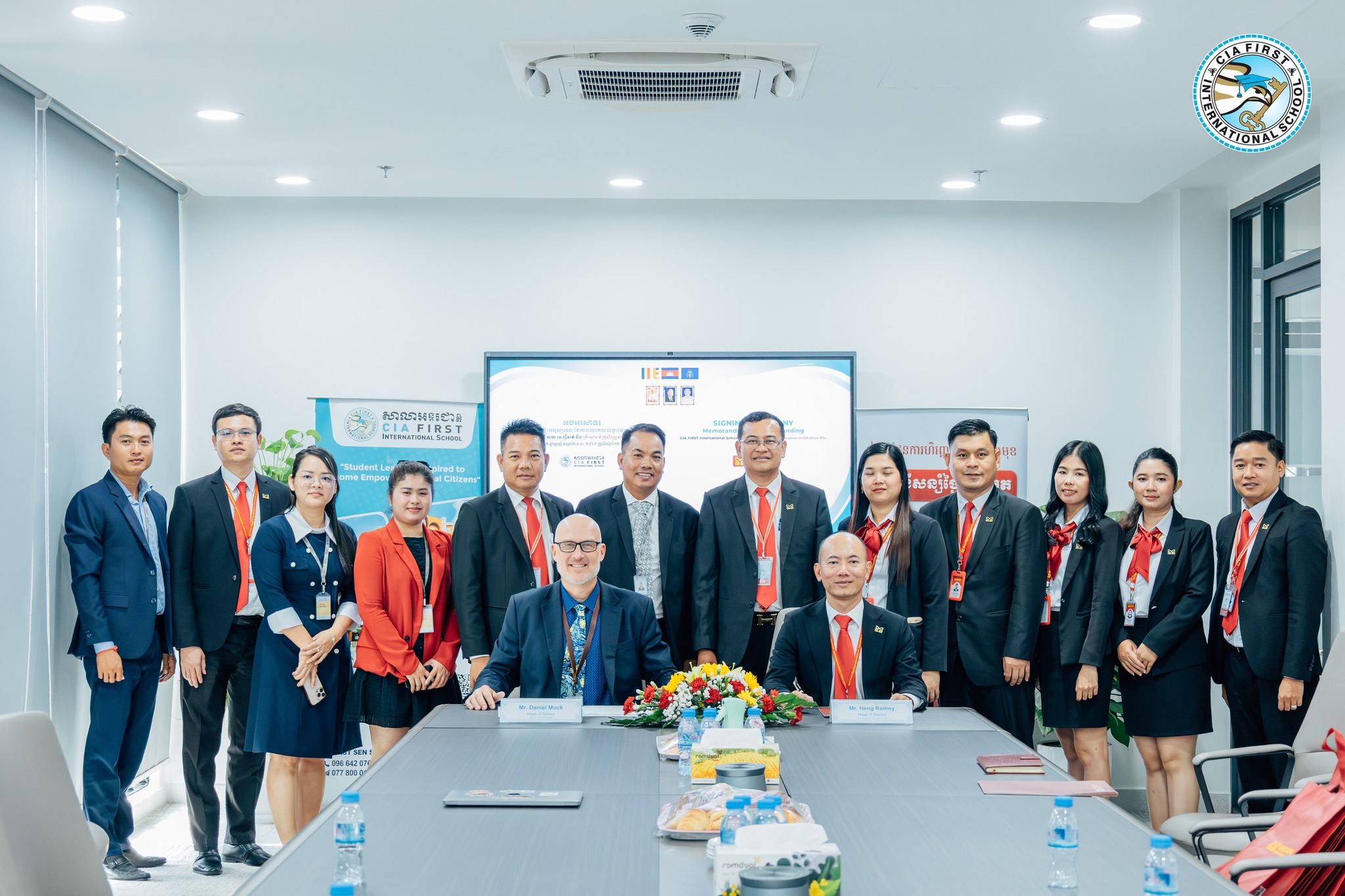 Leaders from CIA FIRST International School and MOHANOKOR Microfinance Institution Plc. signing an MoU during a formal meeting, surrounded by staff.