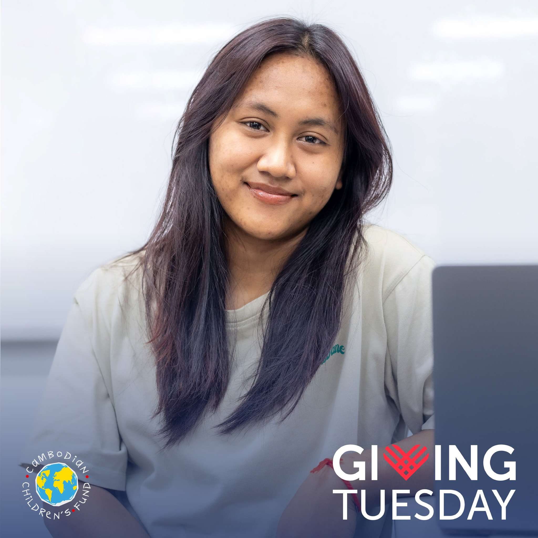 A young Cambodian female student smiling while using a laptop, representing the Cambodian Children’s Fund Giving Tuesday campaign.