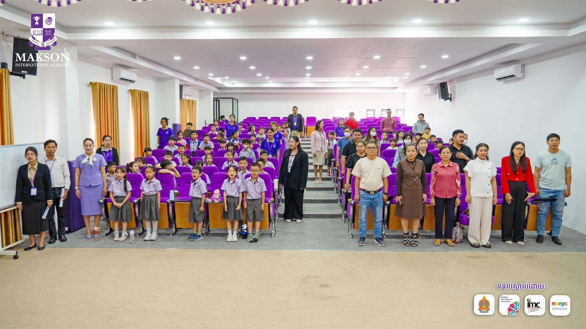 Students and staff at Makson International Academy attending a Khmer spelling competition event with certificates and stage setup.
