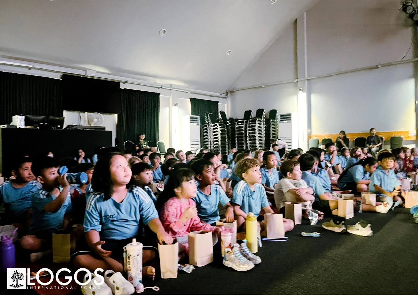 Students attending a movie night fundraiser at Logos International School, sitting together and enjoying a film in a school hall